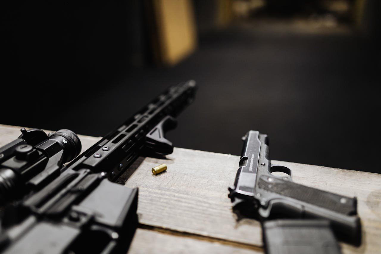Detailed view of a rifle and handgun on a table at an indoor shooting range.