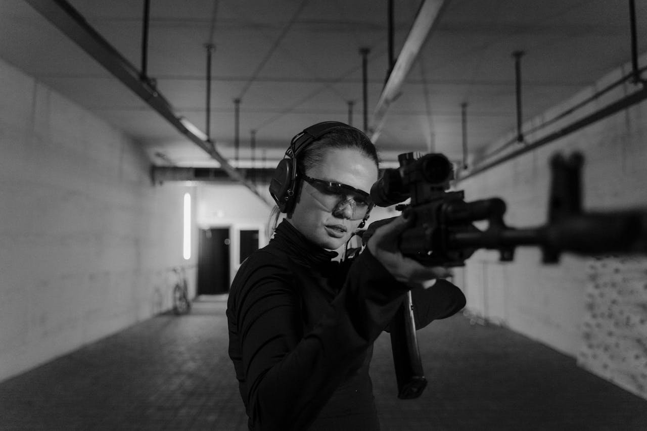 why-choose-us Focused woman aiming with a rifle at an indoor shooting range in black and white.